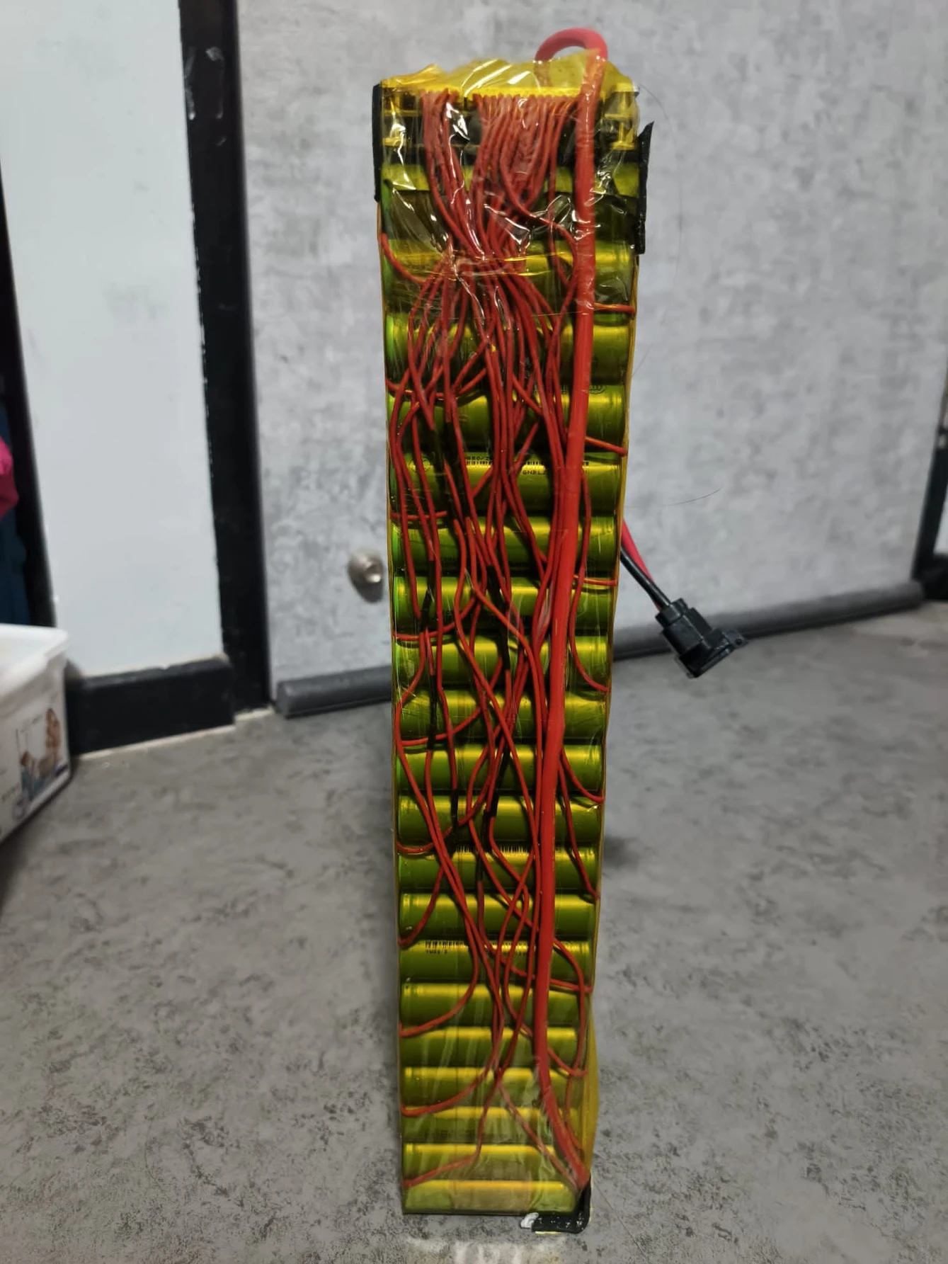 A tall film-wrapped pack with loose red wires down one side and no visible label.