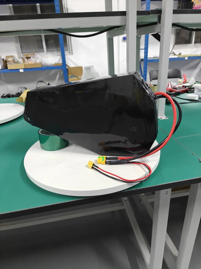 A wrapped black battery pack with an angled, tapering outline and red and black leads, on a turntable.
