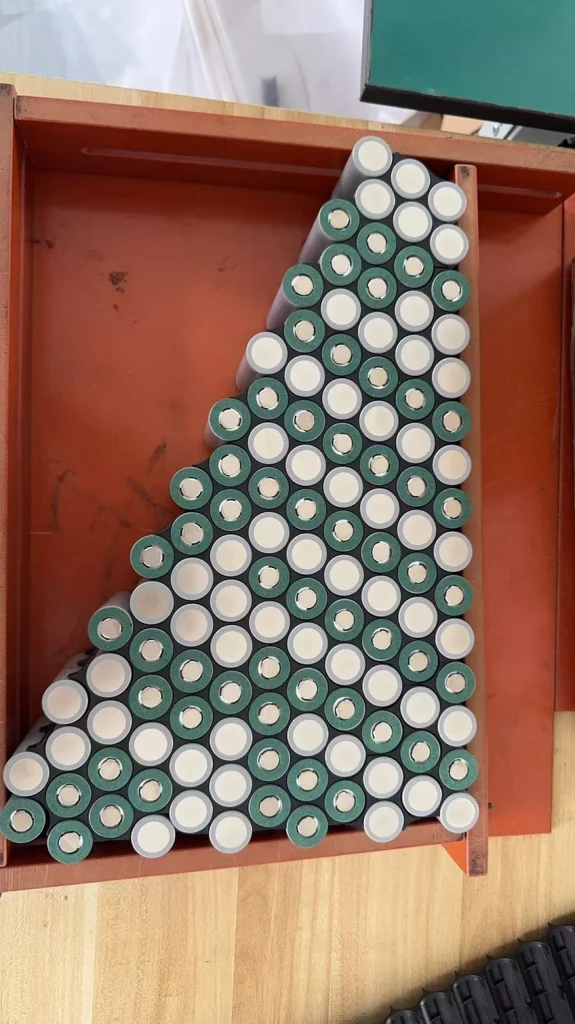 Cylindrical cells laid out in a triangular pattern inside a wooden jig.