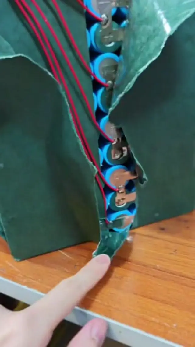 A single column of blue-sleeved cells joined by small nickel strips, with a red balance wire soldered at each step, barley paper pulled aside