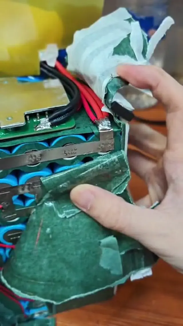 Thick red and black leads soldered onto a small tab at the end of the nickel strip under the BMS