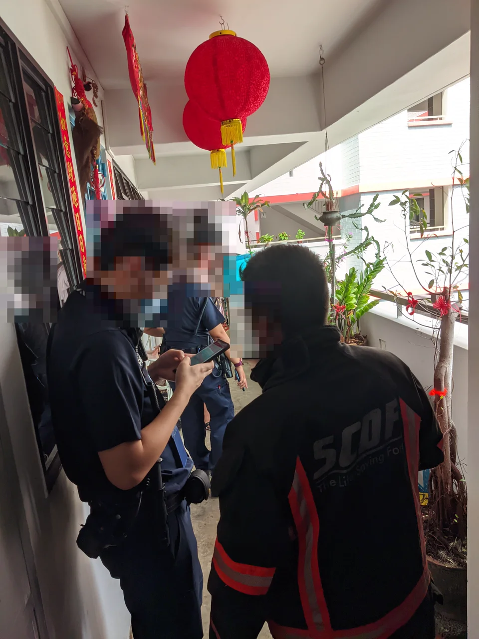 Police officers and an SCDF officer in the HDB corridor, faces pixelated