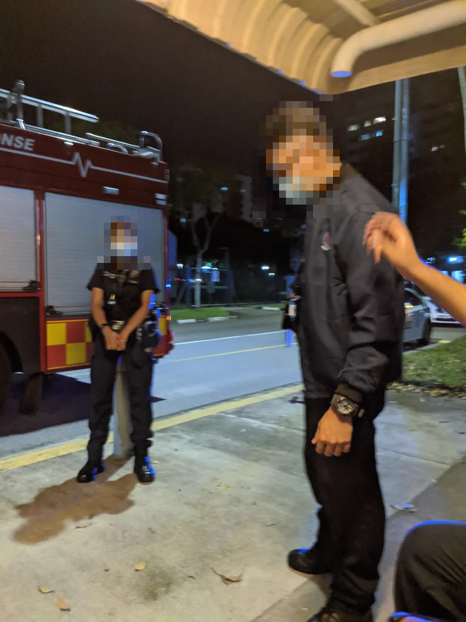 A fire engine at the roadside at night, an officer and a man standing by; faces pixelated