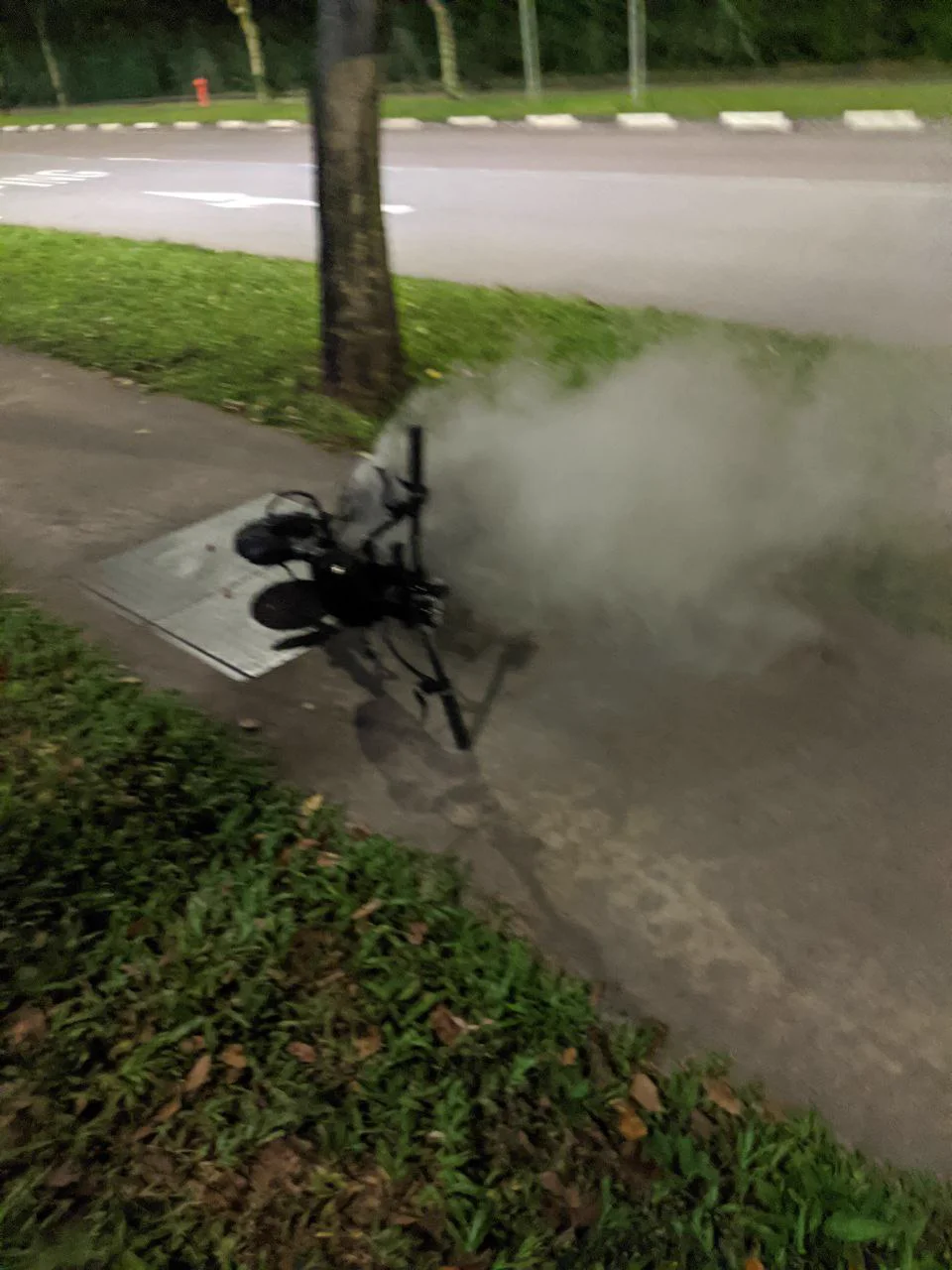 E-scooter on its side on a pavement, smoke pouring from the deck