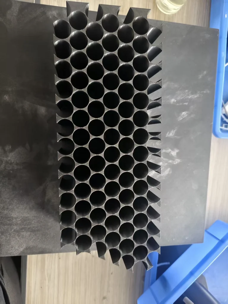 Detached black cell holder with staggered cylindrical channels and walls between them.