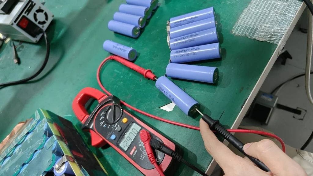 Purple-sleeved cells being measured with a meter on the workbench