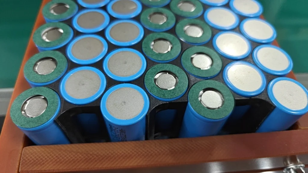 Blue cells in a holder, some ends already fitted with green insulation rings and some still bare