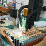 A spot welder firing over copper busbars on a pack held in a jig