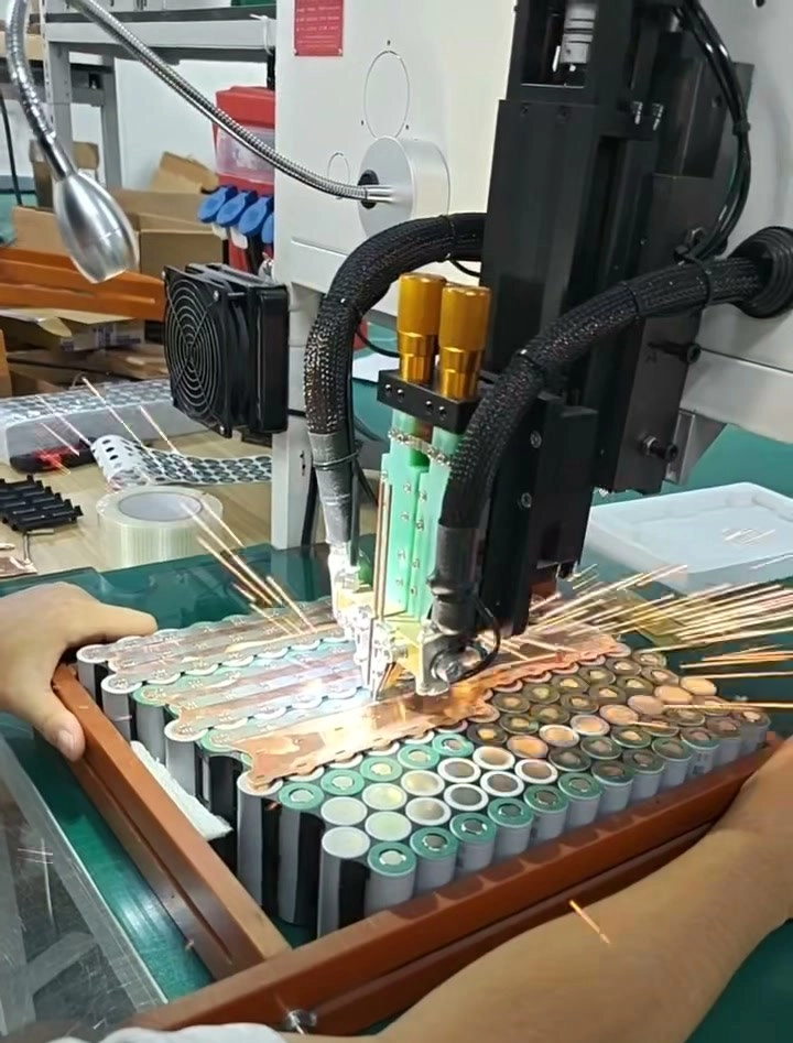Spot welder firing sparks over copper busbars on a pack held in a jig
