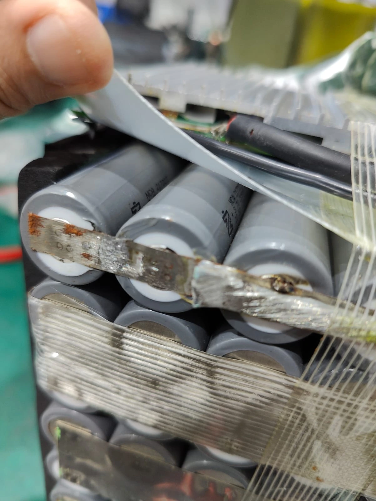 Close-up of a metal strip connecting cylindrical cells with brown marks beside the welds.