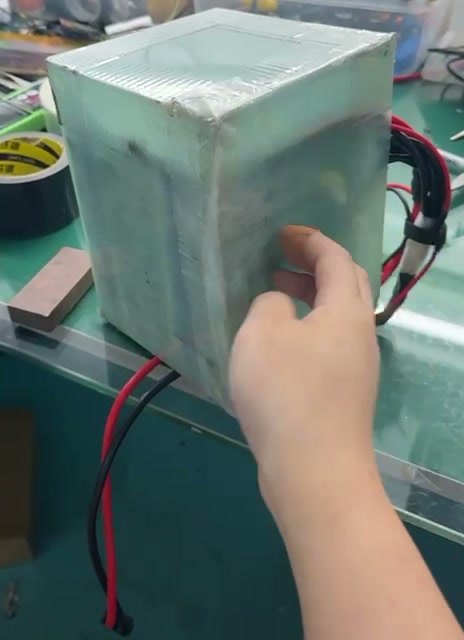 Film and clear tape around the pack, with red and black leads exiting at a lower corner.
