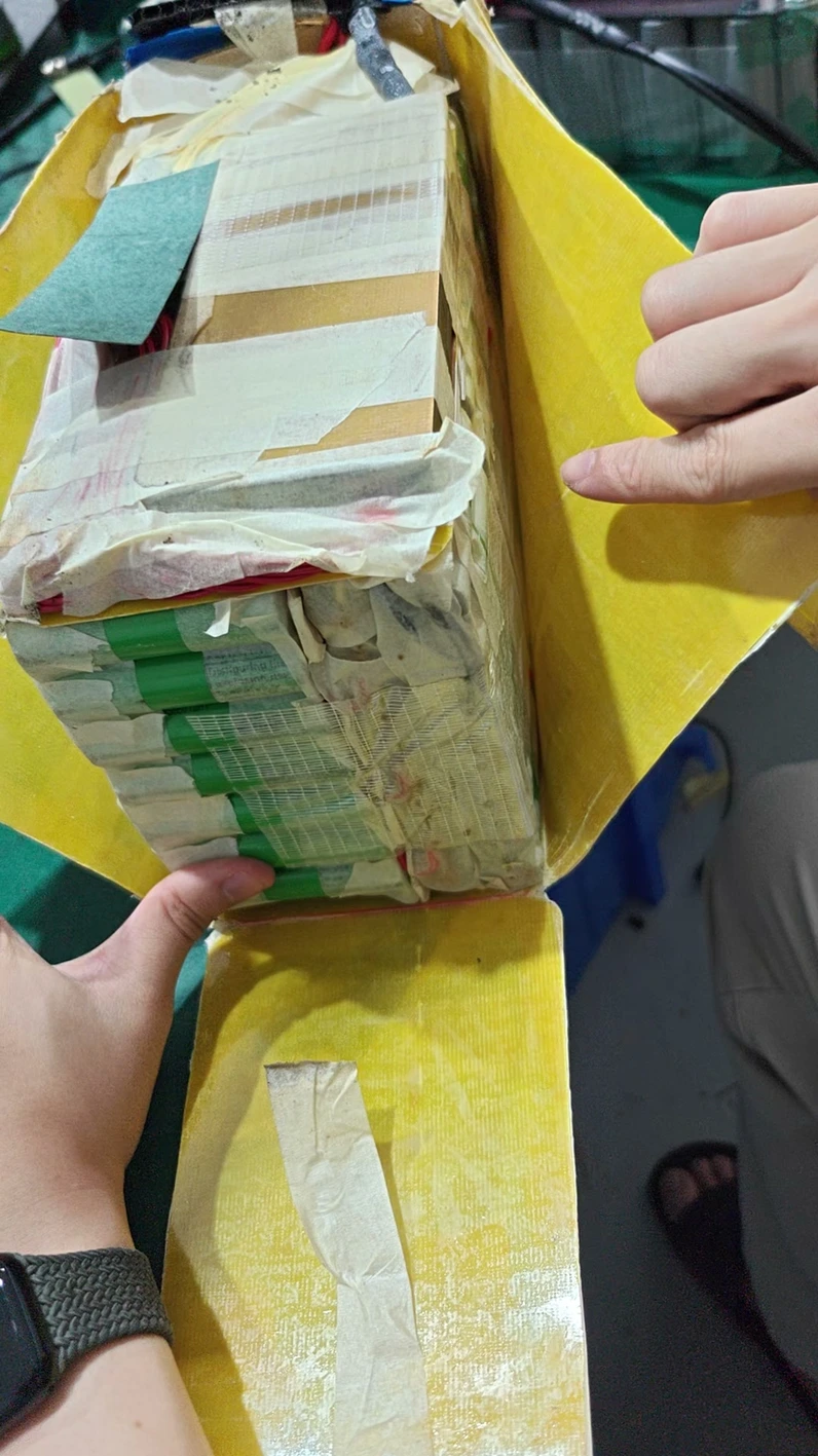 A pack wrapped in layers of tape and yellow paper, being unwrapped by hand.