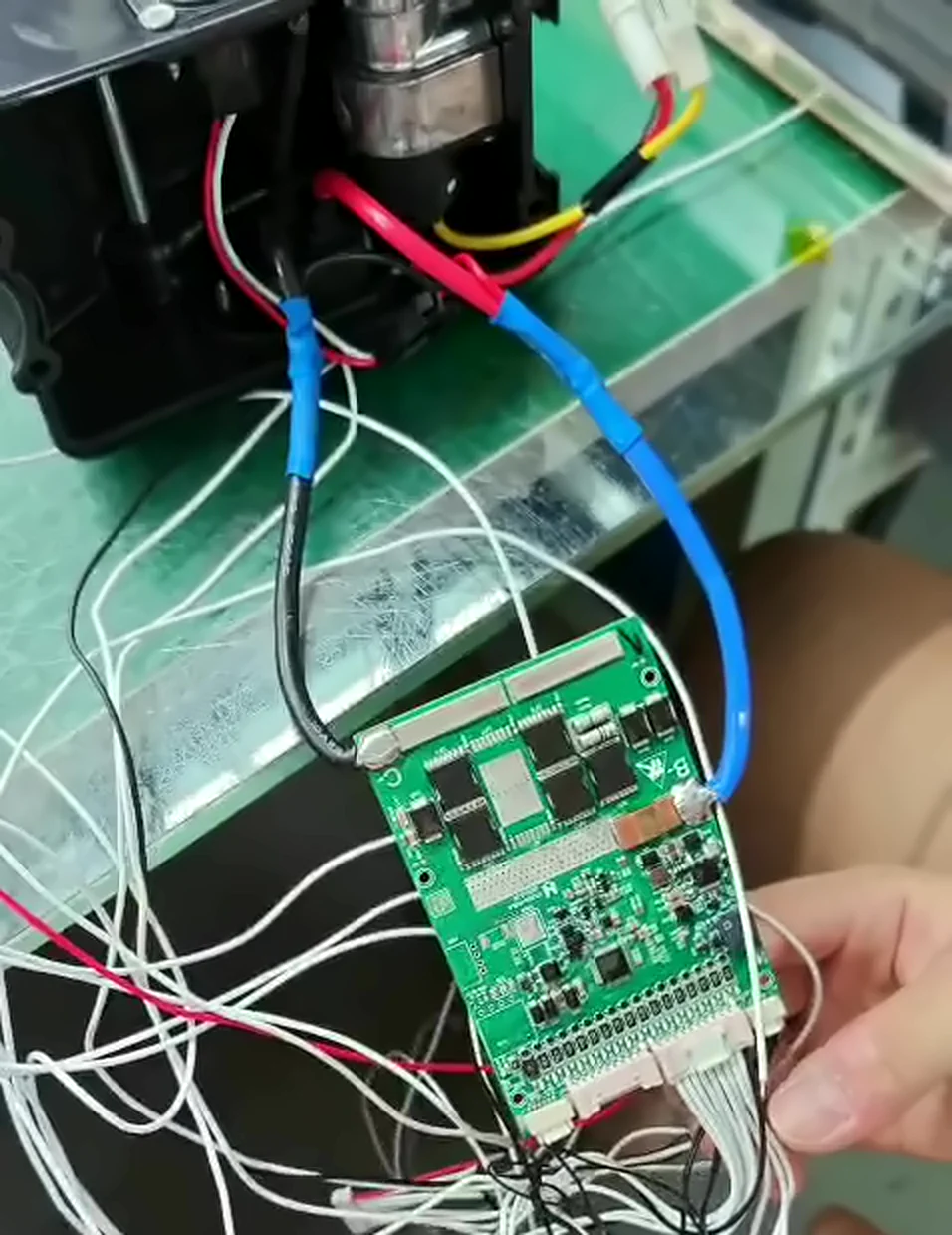 Green BMS board with its black C− lead and blue B− lead both running up into the black connector housing, the blue one joined to a red wire