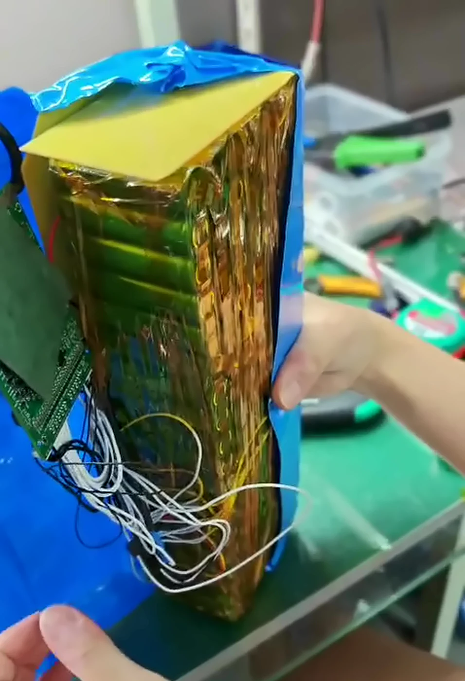 Heat-shrink peeled open: a green BMS board lying against the side of the Kapton-taped cells, balance wires tangled below