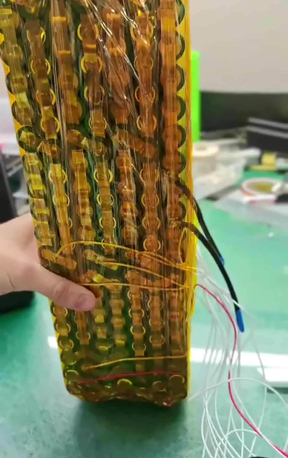 Kapton-taped cell block with blue-tipped black leads and white balance wires hanging loose